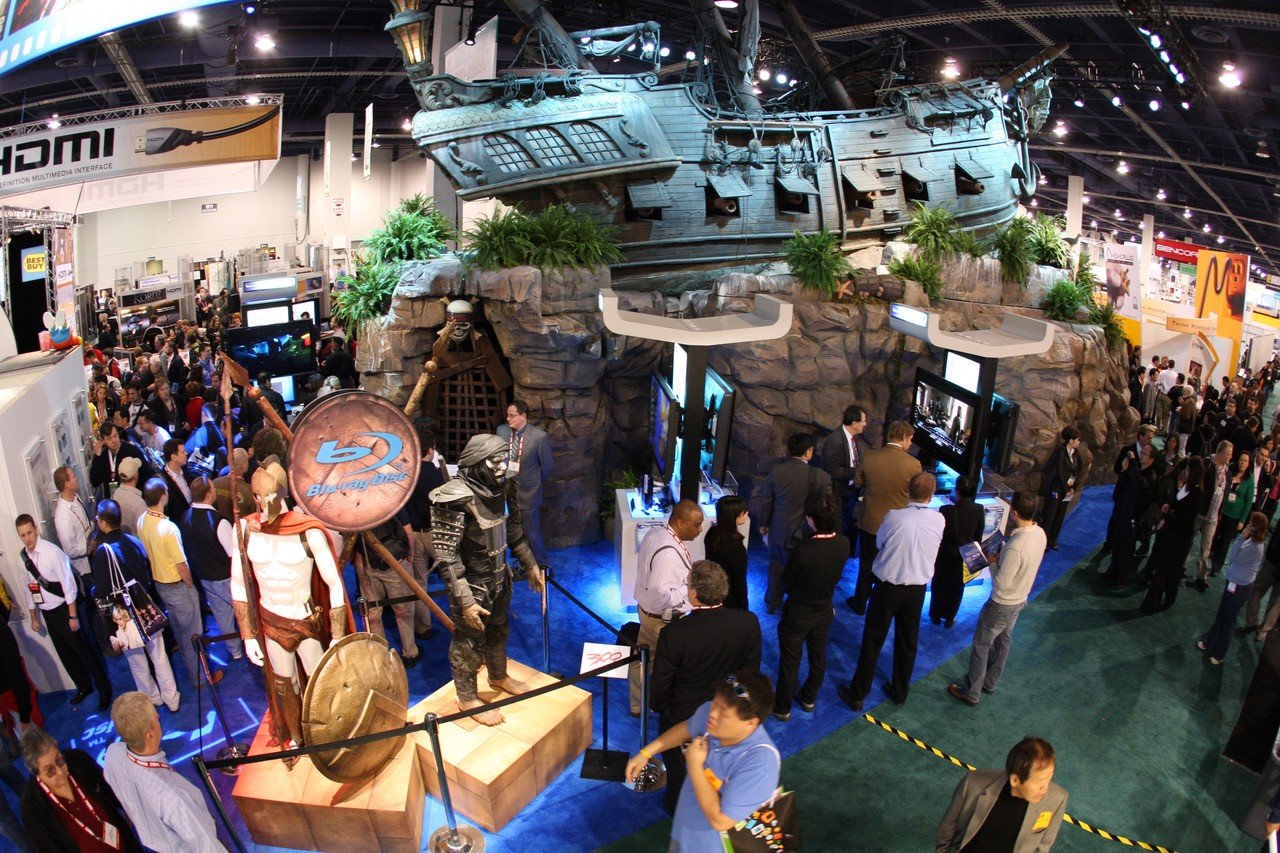 Crowded CES show floor surrounding the Blu-ray Disc Association booth, with a pirate ship installation and movie character statues