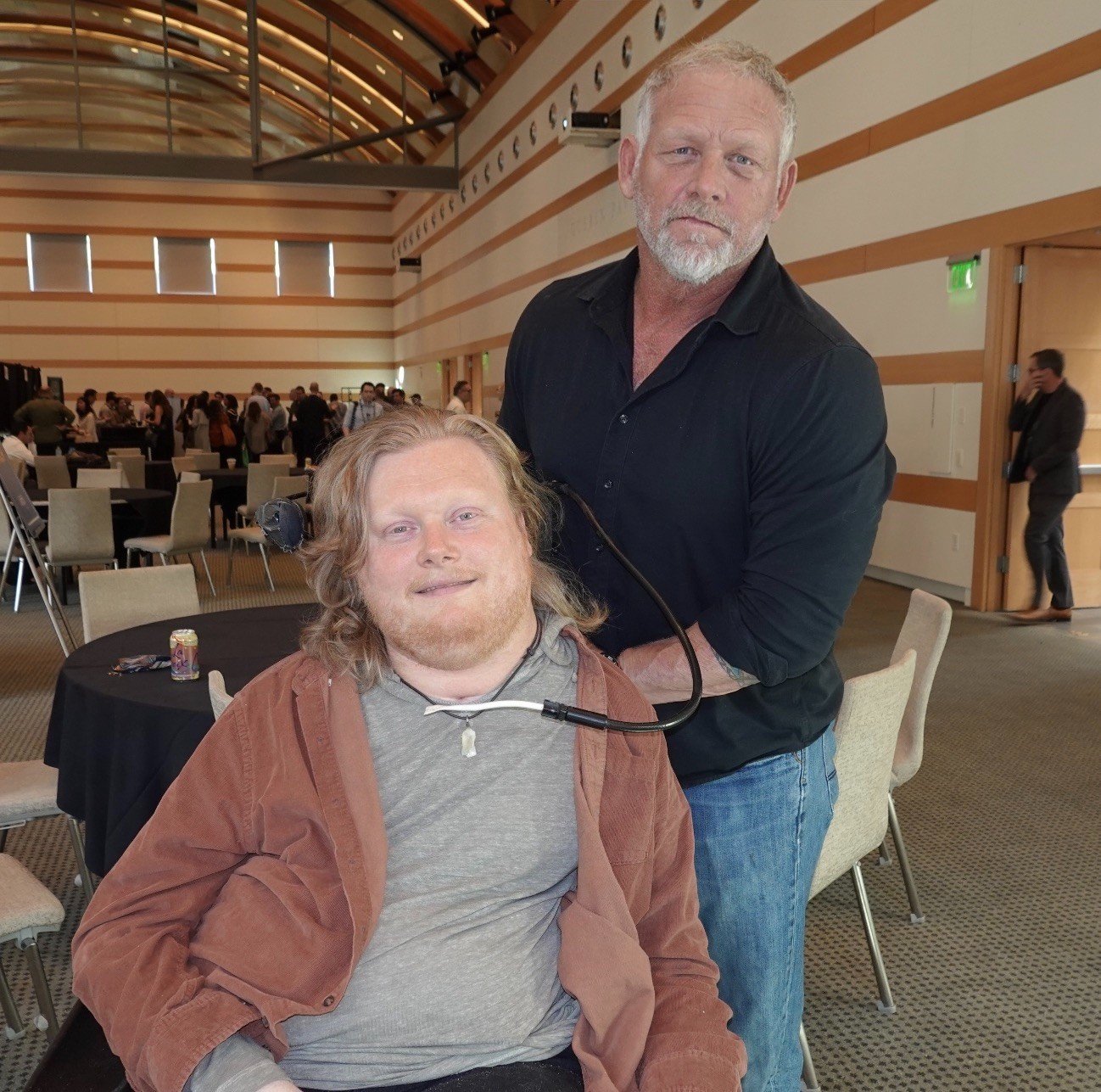 Michael Hoog standing with his son Tyler Hoog, who uses a power wheelchair, at an industry event